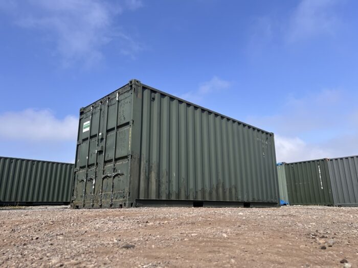 Low angle photo of a 20ft ex-hire green shipping container in outdoor yard on a clear day