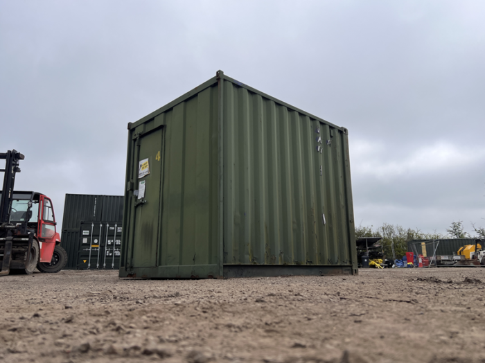 Ground-level view of green 8ft storage container on gravel surface with cloudy sky
