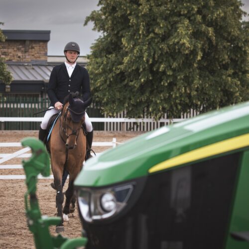 questrian rider on a bay horse passing a John Deere tractor at the showground.