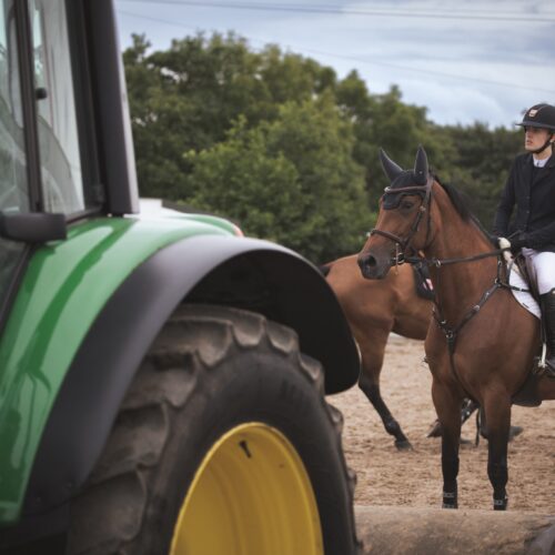 Equestrian competitor waiting near a green tractor at the warm-up area.