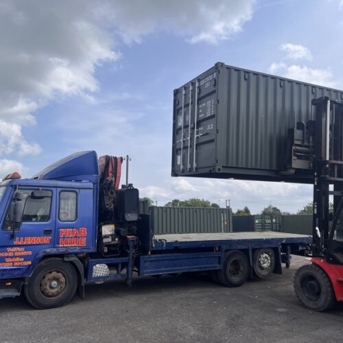 Green shipping container mid-air being loaded by forklift onto a HIAB lorry at the Darlington A66 depot.
