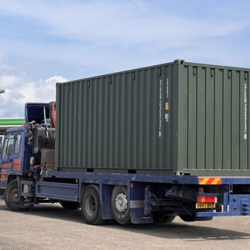 Fully loaded HIAB lorry leaving the depot with a green shipping container onboard.